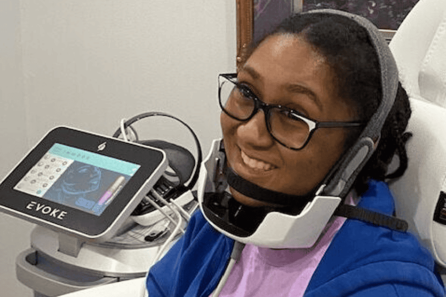 young woman in a blue aweater and pink shirtsmiling while she is receiving a facial treatment