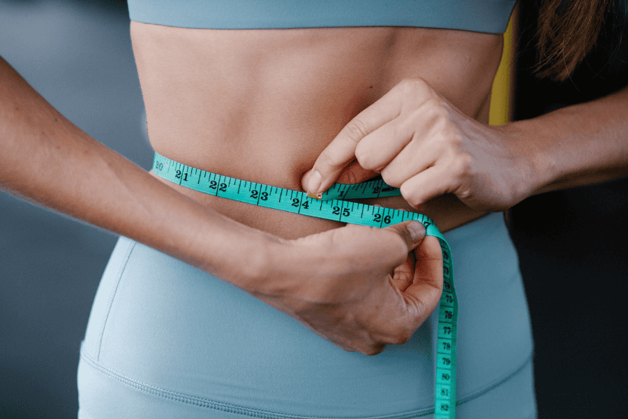 woman in a teal workout outfit measuring waist