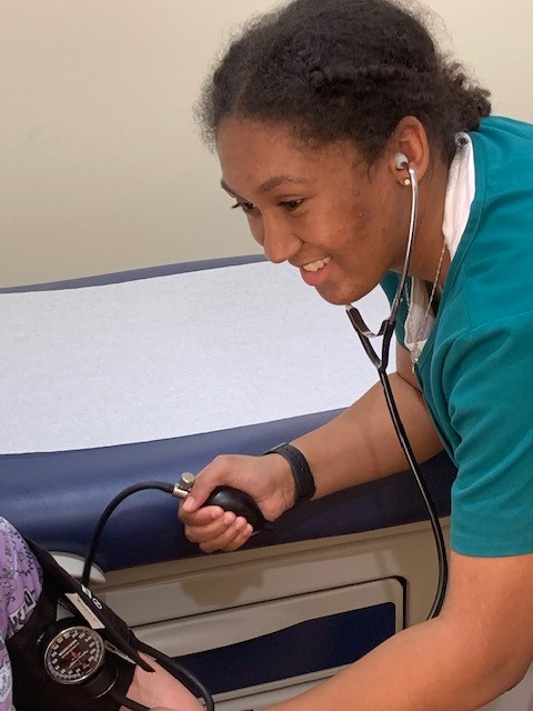 Attractive African American medical assisstant in green scrubs taking blood pressure