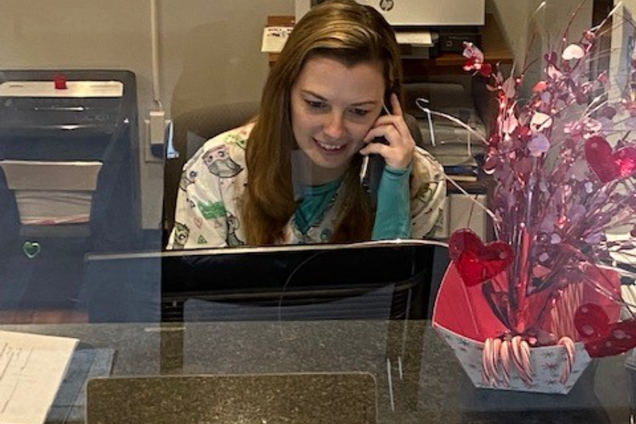 Young caucasian female in scrubs answering phone at front desk of Pro Health Services